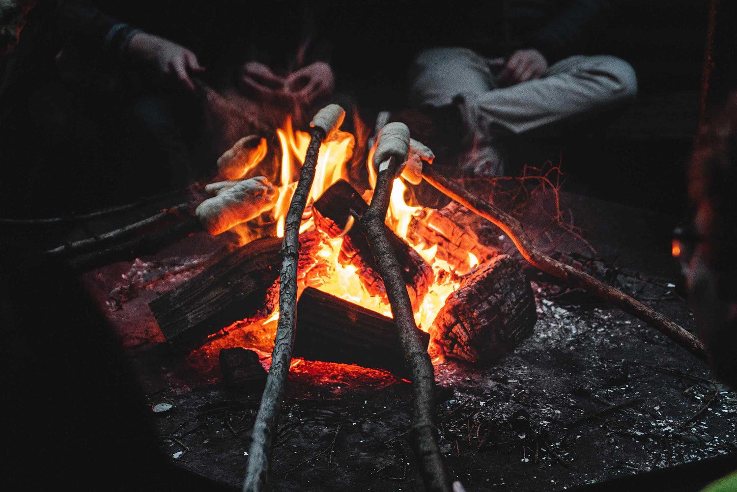 A bonfire where some are sitting and baking stick bread.