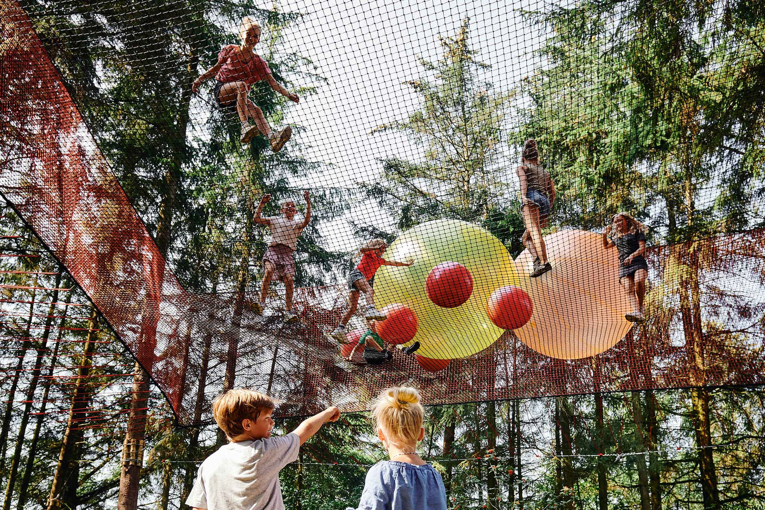Ein Junge und ein Mädchen stehen auf dem Boden. Der Junge zeigt nach oben auf andere Kinder, die in einem Netz im WOW PARK spielen.