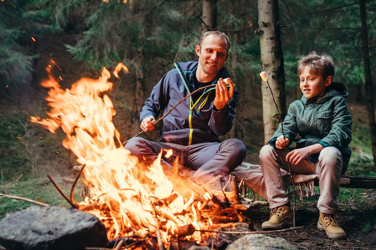 Vater und Sohn sitzen im Wald am Lagerfeuer und machen S’mores.