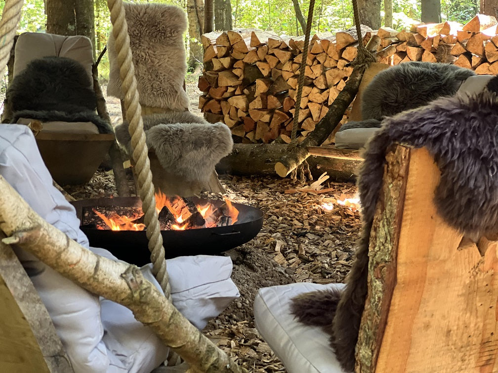 Træstole med skind omkring et tændt bålfad i Campen i WOW PARK.