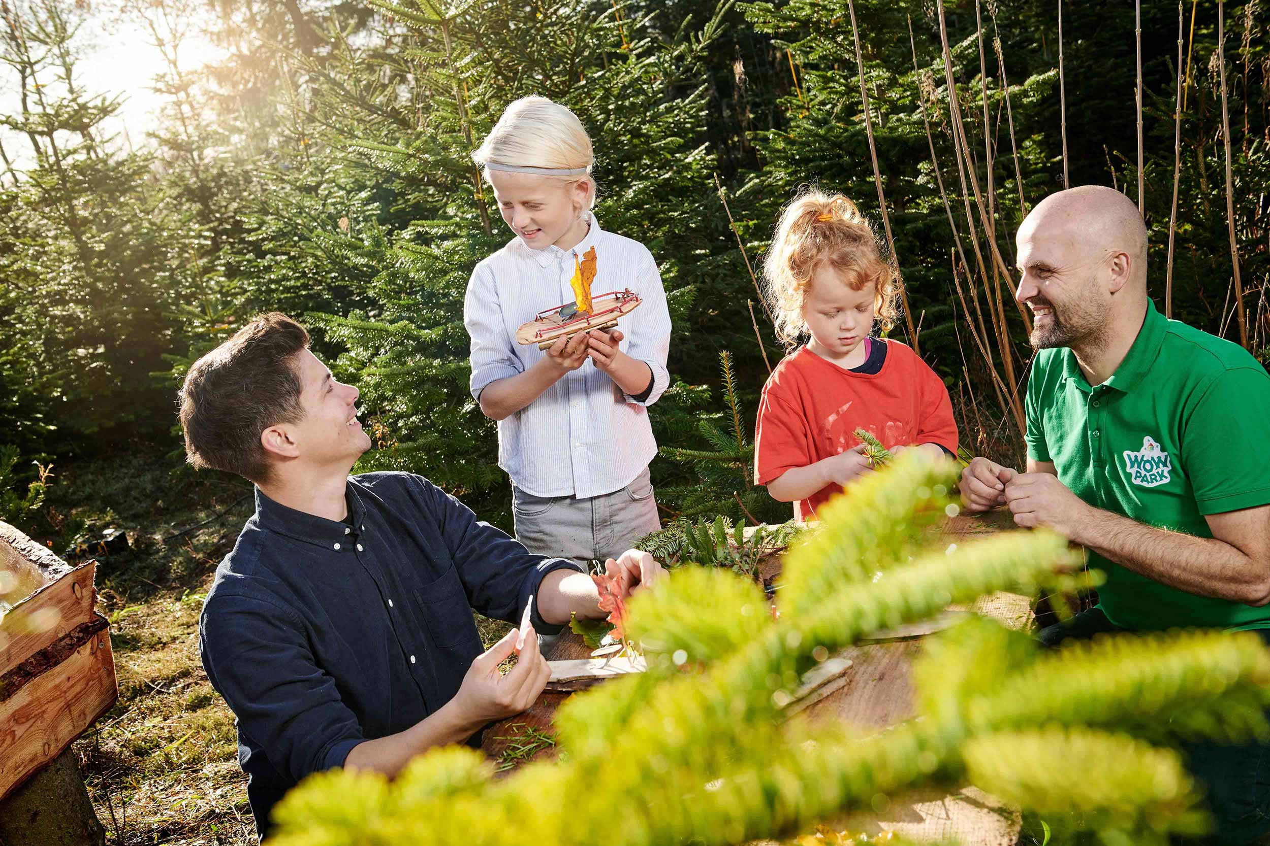 To mænd og en dreng og en pige hygger sig med en aktivitet i WOW PARK i skoven.