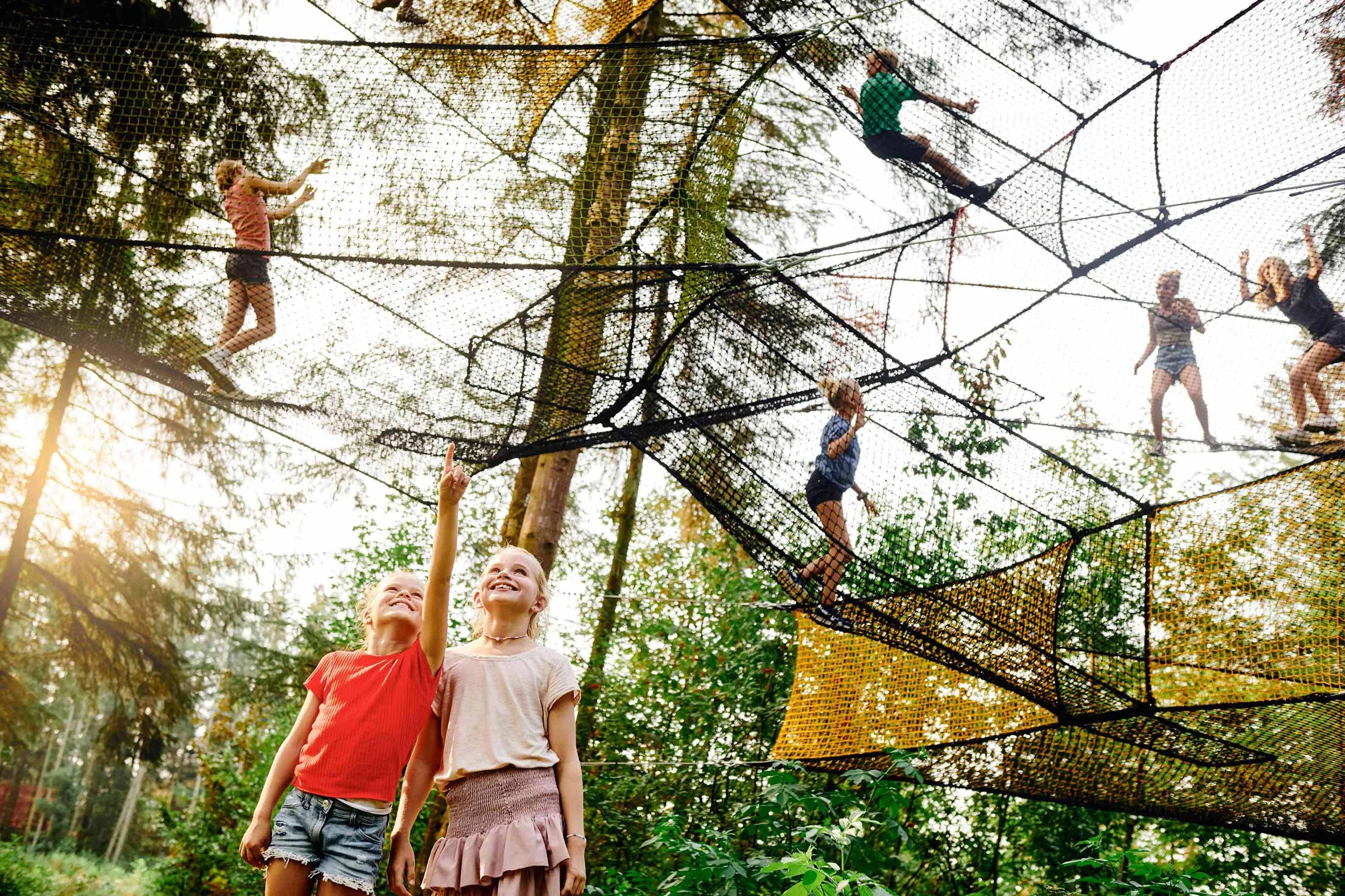 Children are playing in the nets at WOW PARK, while other children are looking up at them.
