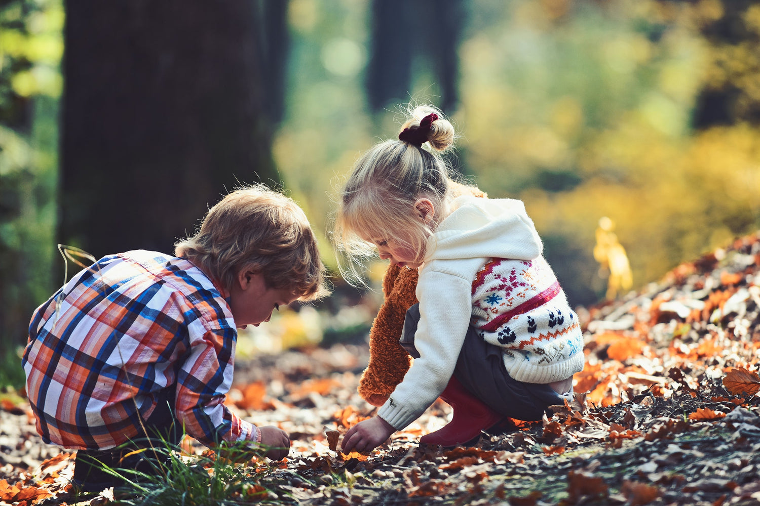 Two children are enjoying themselves sitting and searching for things on the forest floor.