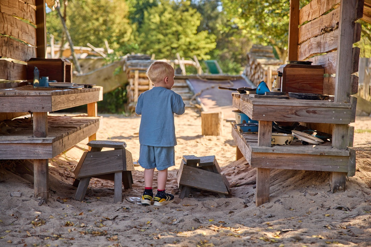 A little boy stands with his back turned, looking at a play kitchen in WOW PARK. The sun is shining.