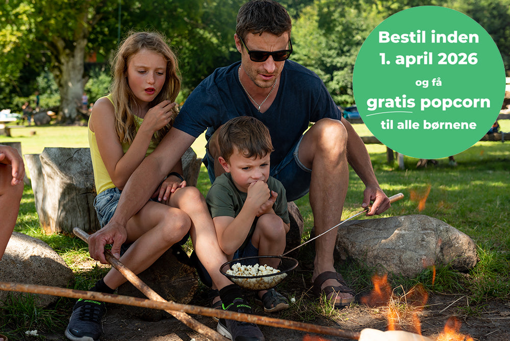 En far og to børn sidder ved et bål i WOW PARK og tilbereder popcorn.