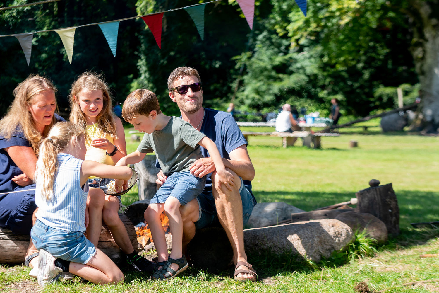 En familie sidder sammen i WOW PARK Skjern. Det ser ud som om, at de lige har tilberedt popcorn på bålet.