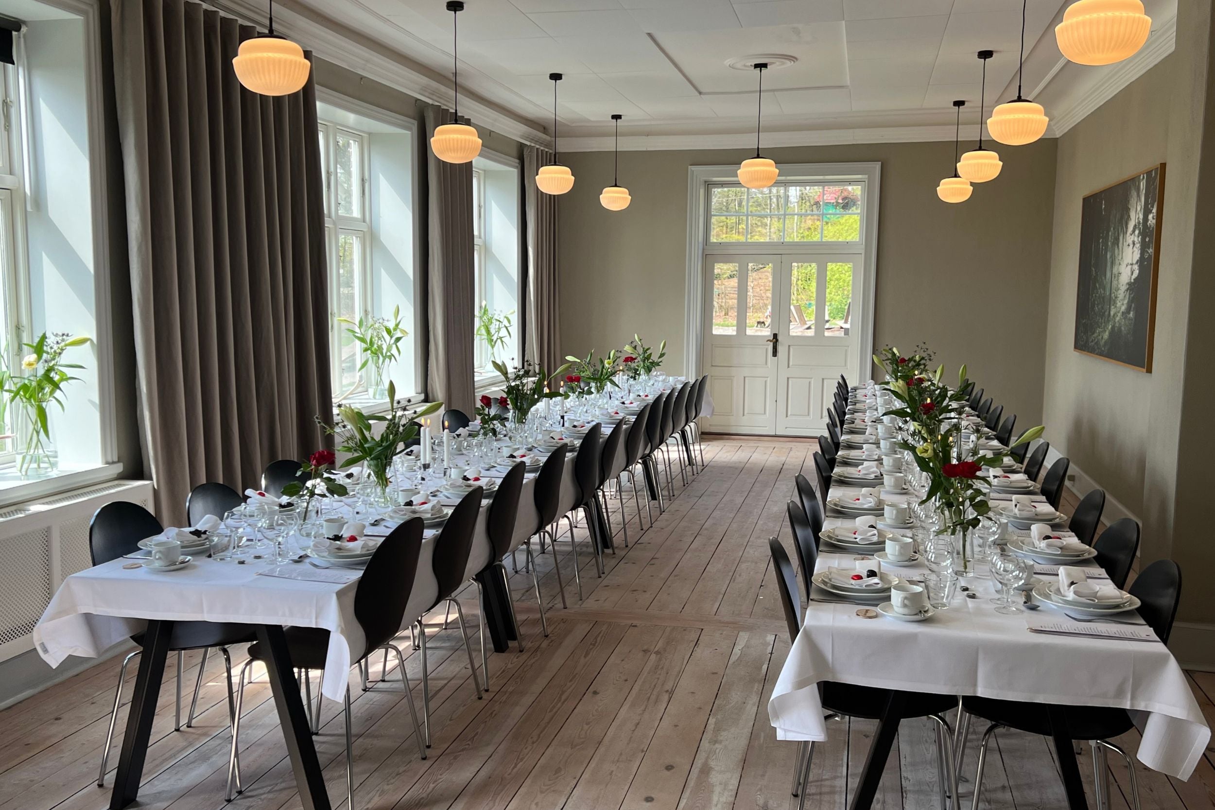 Festlokale i WOW PARK Skjern. Man ser to rækker borde, flot dækket op med hvide duge, service og blomster på bordene.