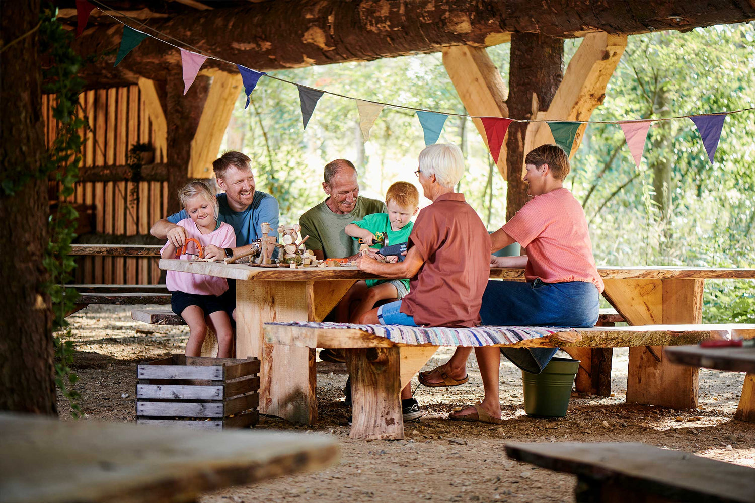 Drei Generationen genießen die Zeit zusammen an Tischen und Bänken im Skovhuset im WOW PARK Billund.