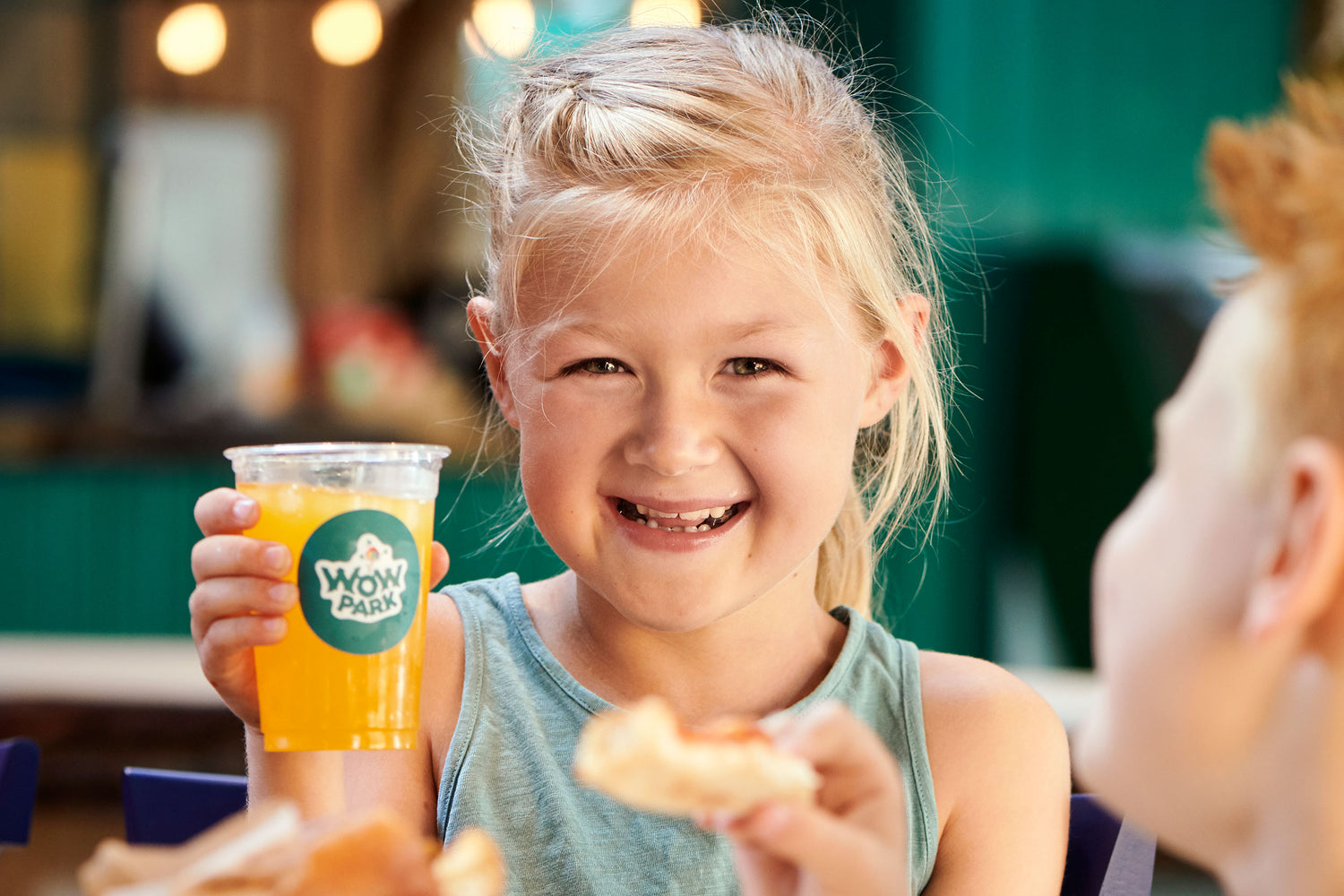 Two children are enjoying themselves in the food court Madladen at WOW PARK. The girl is sitting with a soda.