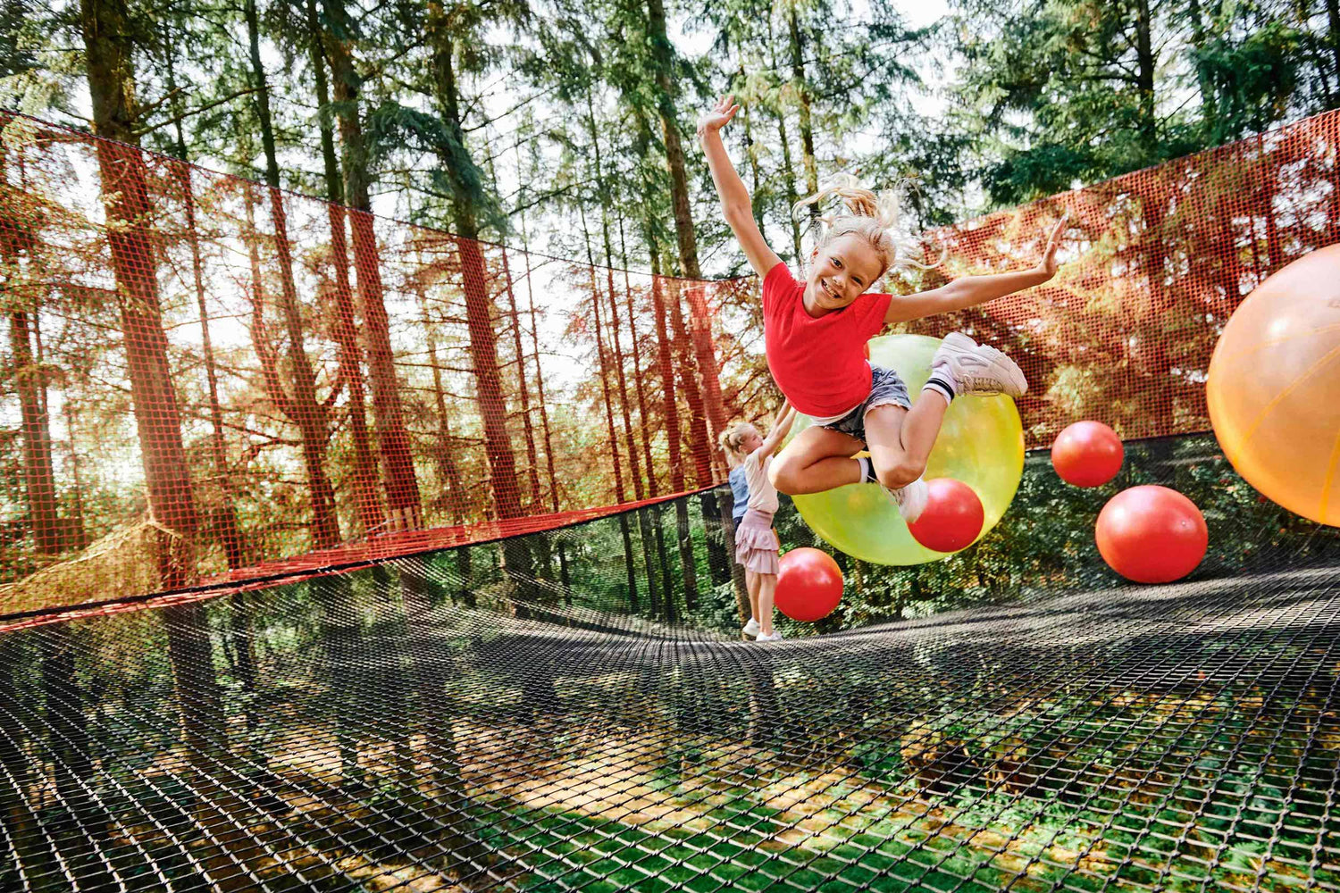 A joyful girl leaps into a giant net, surrounded by colorful balls.