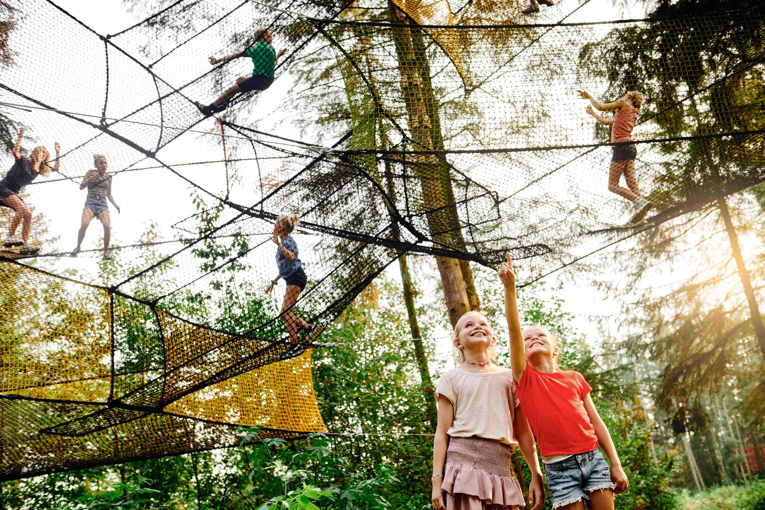 Children are playing in a large net. Two girls are standing and looking up at the net.