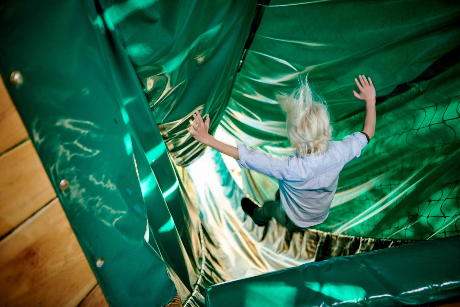 A boy zooms down the slide at full speed, his hair flying back showing just how fast he’s going.