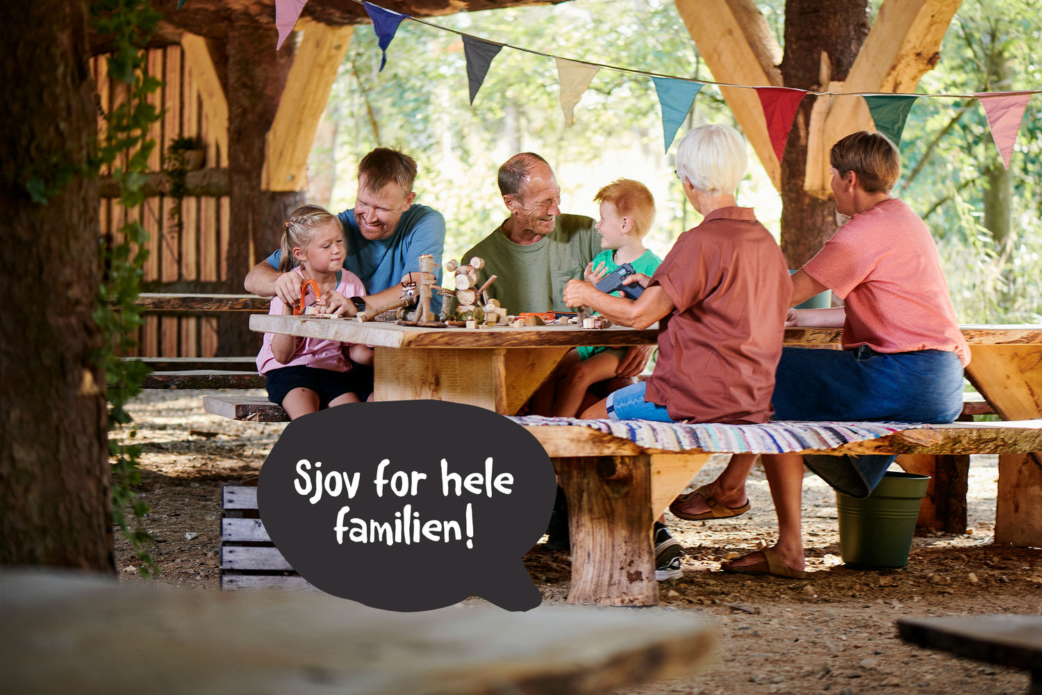 Man ser en familie med 3 generationer, hvor sidder og laver krea ved bord og bænke.