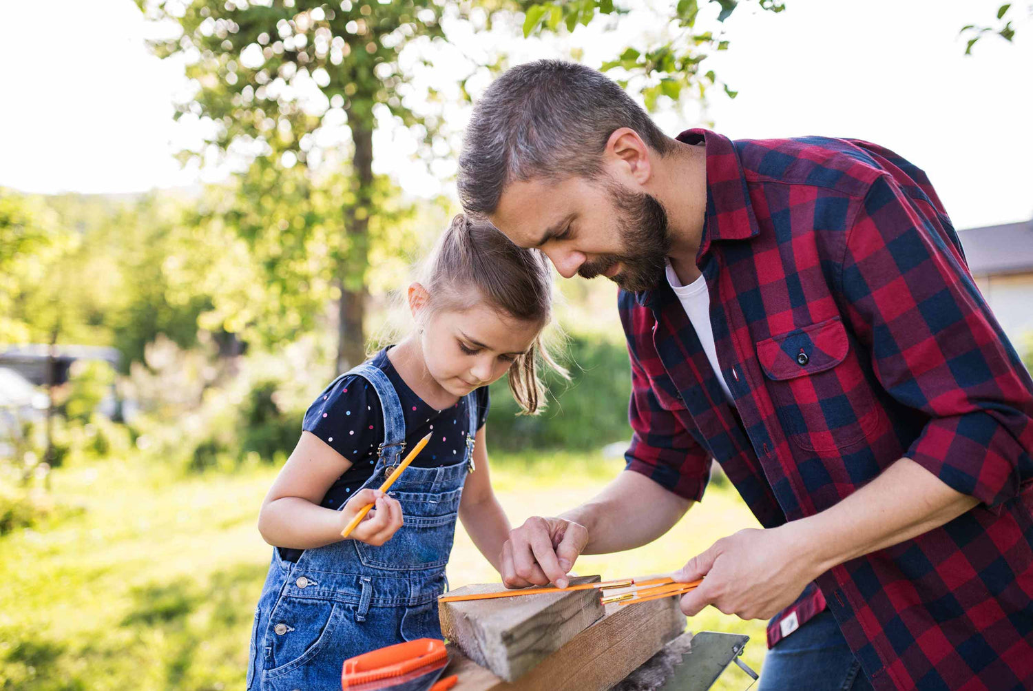 A father and daughter are measuring something on a piece of wood.