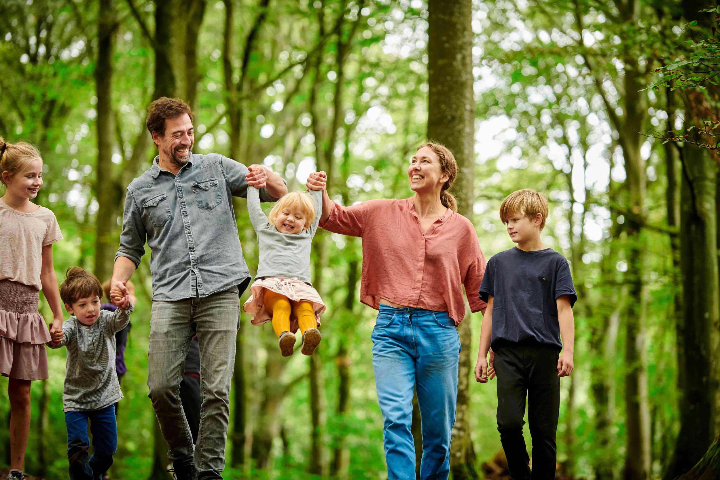 En familie på seks personer, hvor de fire er børn, går i WOW PARK mellem de lysegrønne træer.