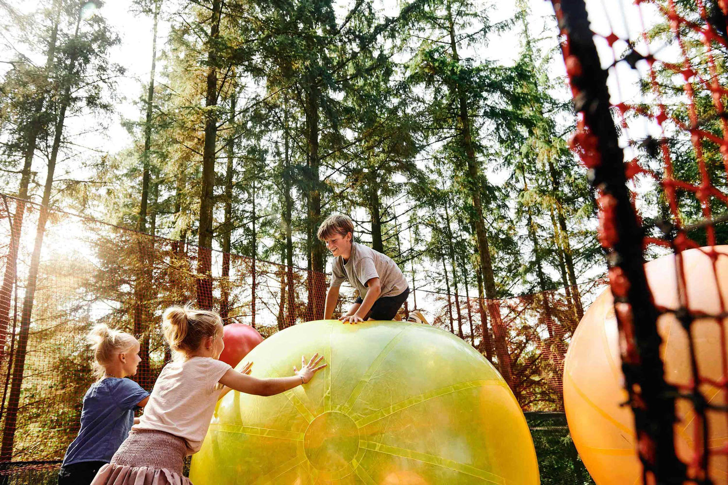 Children are playing with large balls in different colors in a big net. A boy is sitting on top of one of the balls.