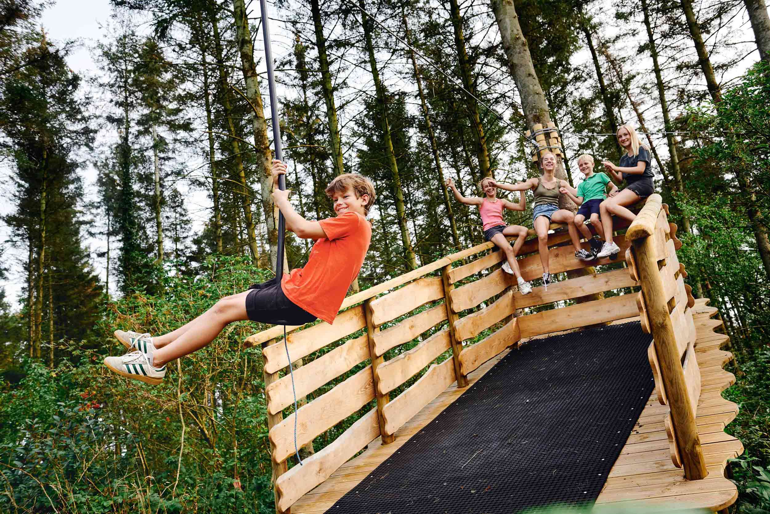 A happy boy wearing a red T-shirt is having fun on a zipline in WOW PARK, soaring out into the air.