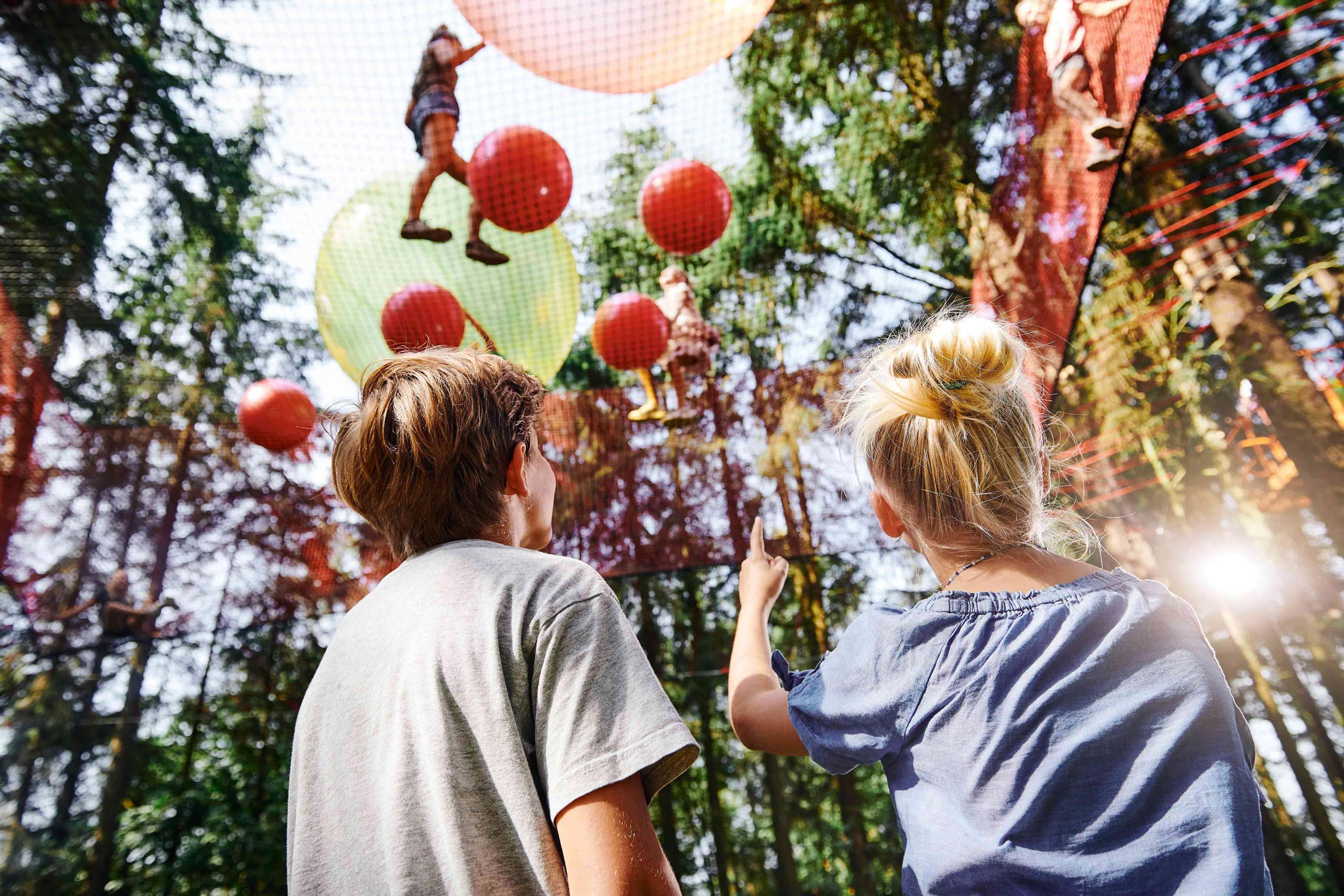 Children playing up in a net with balls. Two other children are watching them from below.