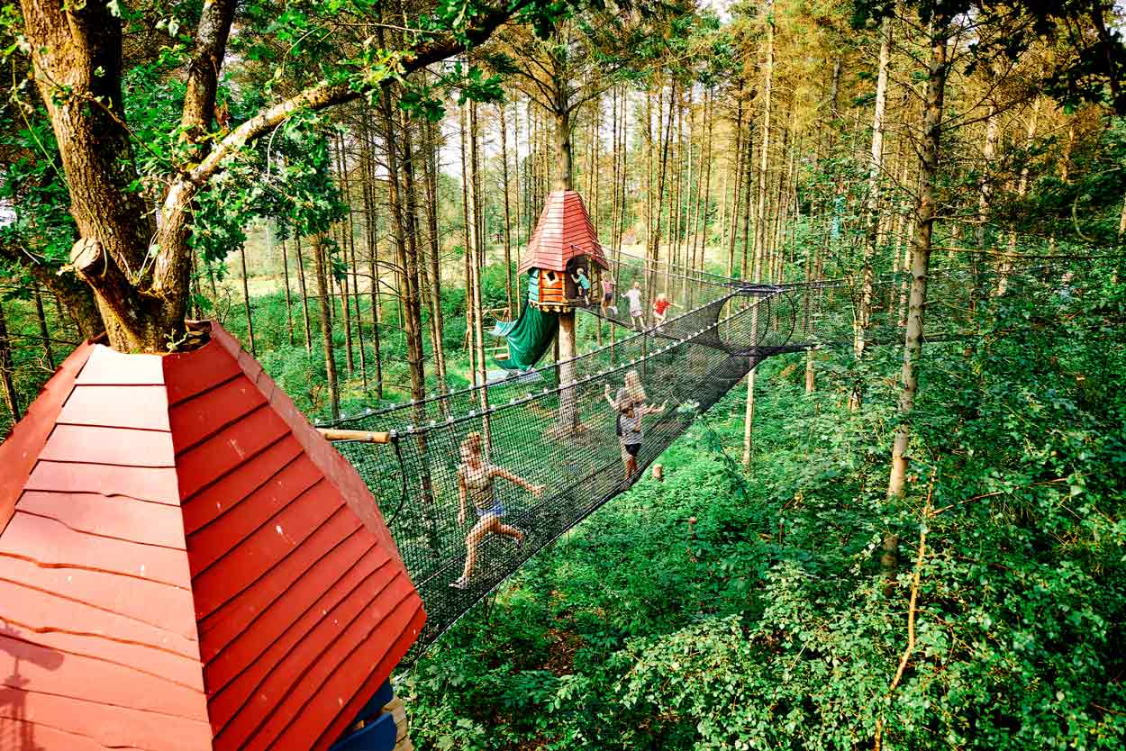 Treetop huts and net walkways high up in the air at WOW PARK. You can see children walking on the walkways.